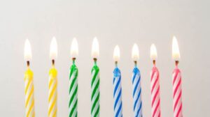 Is your pension age changing? Image depicts a row of 8 birthday candles, in yellow, green blue and red. All 8 candles are lit.